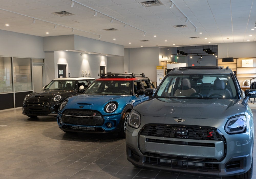 Three Mini Cooper cars, gray, blue, and black, lined up inside a modern car showroom.