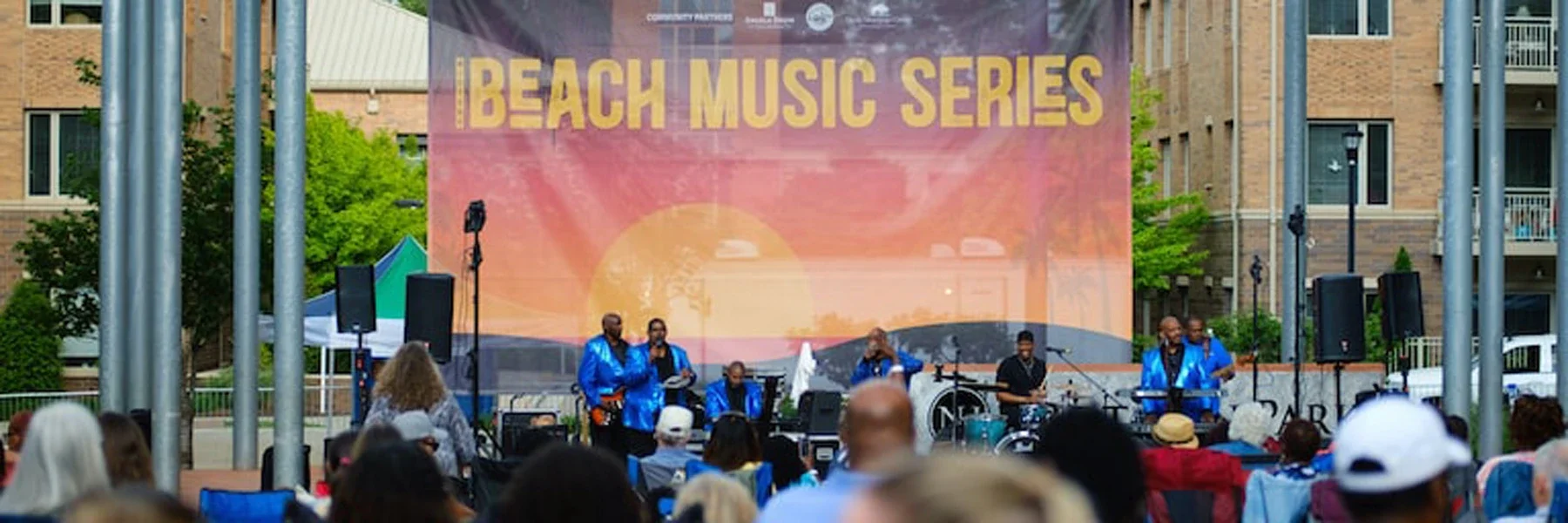 A band in blue performs on stage with 'IBEACH MUSIC SERIES' banner, while an audience watches.
